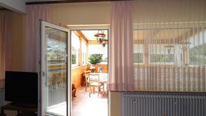 An open sliding glass door leading to a dining area with a table and chairs, a radiator, and a television on a stand. - Vacation home Anna by Interhome (Issigau)