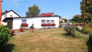 A white two-story house with a red roof, surrounded by a well-maintained lawn and potted plants. - Vacation home Anna by Interhome (Issigau)