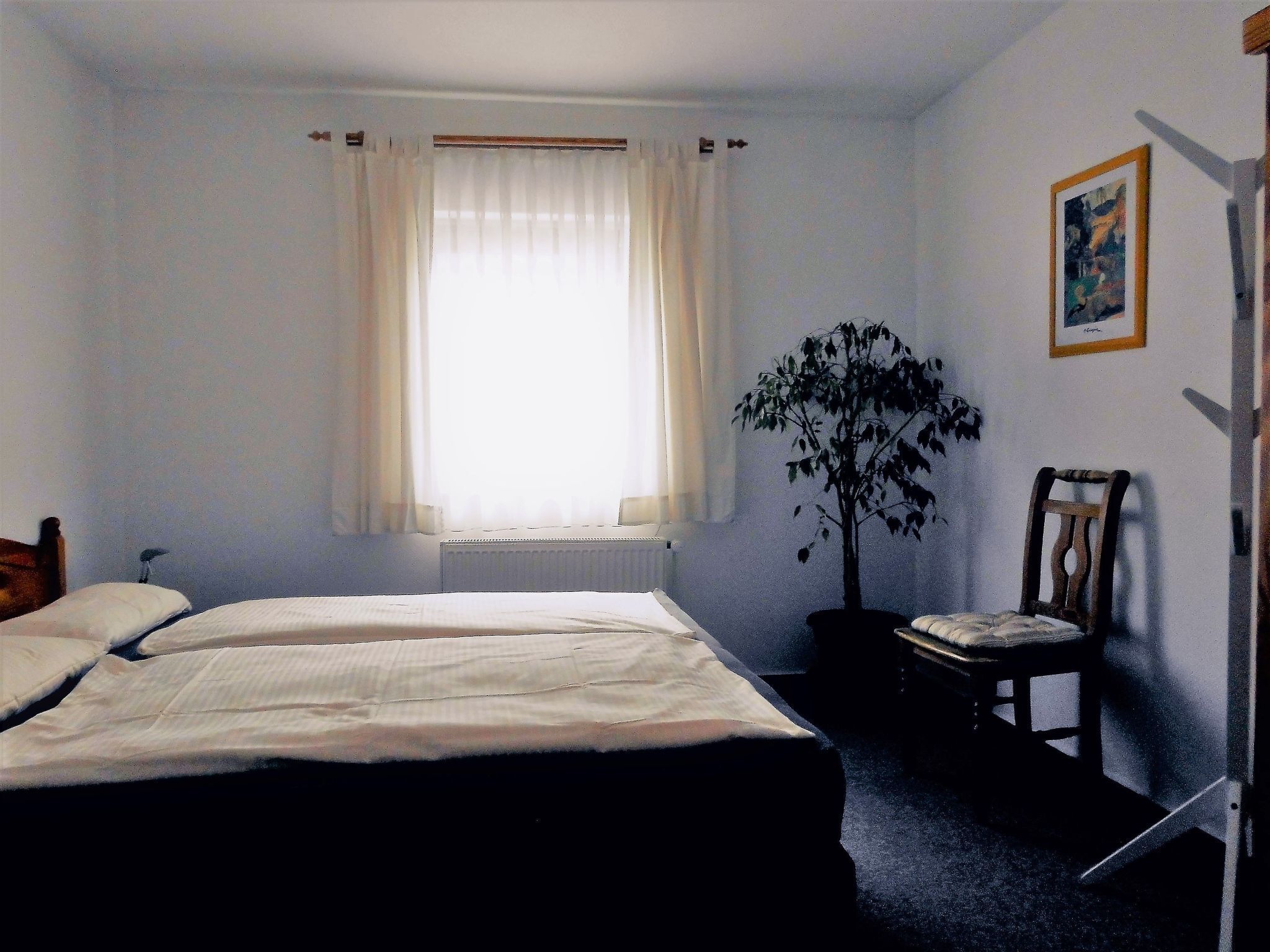 A room with two beds, a radiator, a window with curtains, a chair, and a wall-mounted picture.