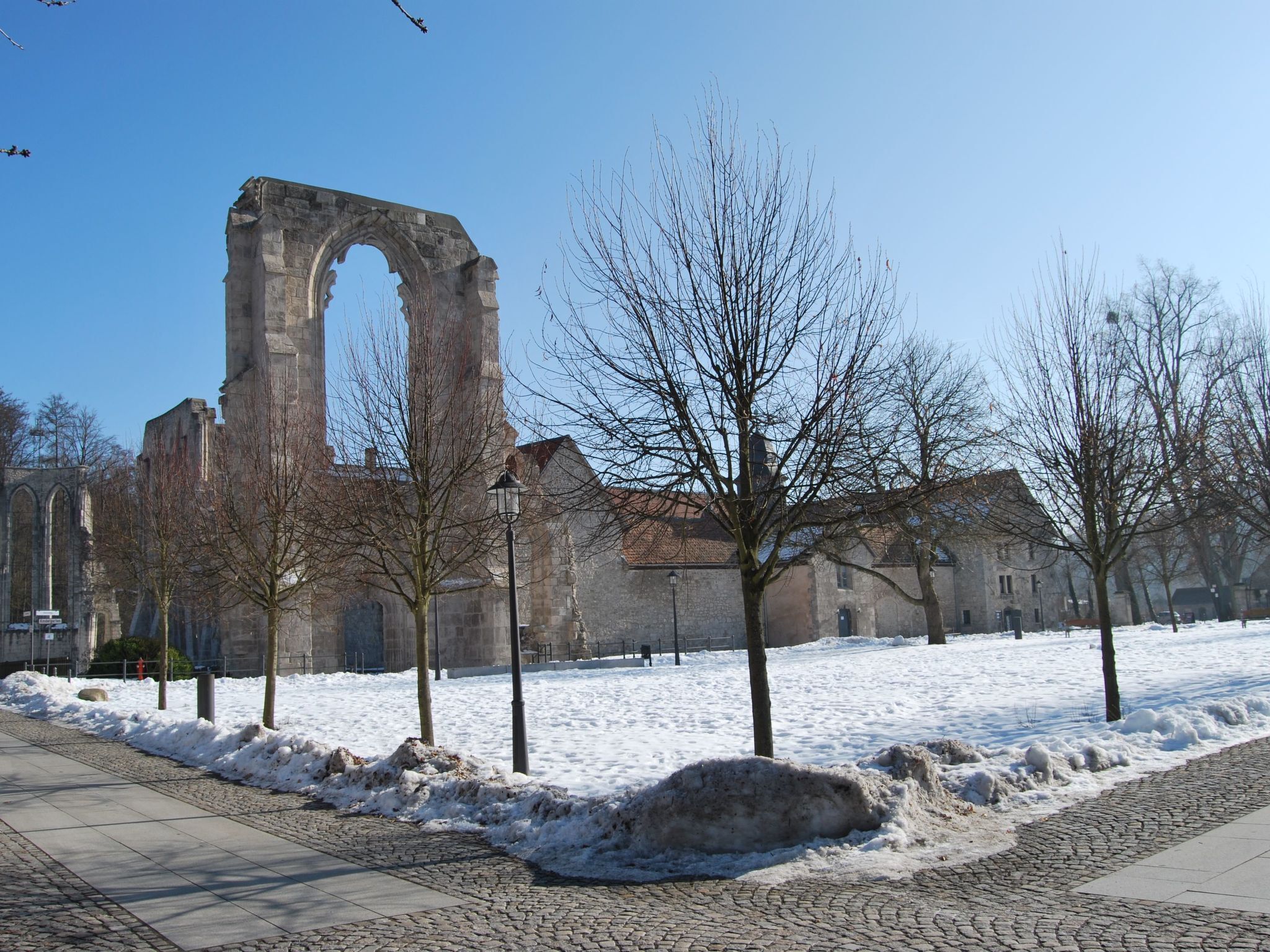 Una estructura de piedra histórica con un arco, rodeada de árboles desnudos y un suelo cubierto de nieve.