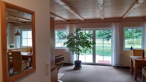 A spacious room with a large window, a potted plant, and a wooden ceiling. - Fewo Stricker 31 by Interhome (Walkenried)