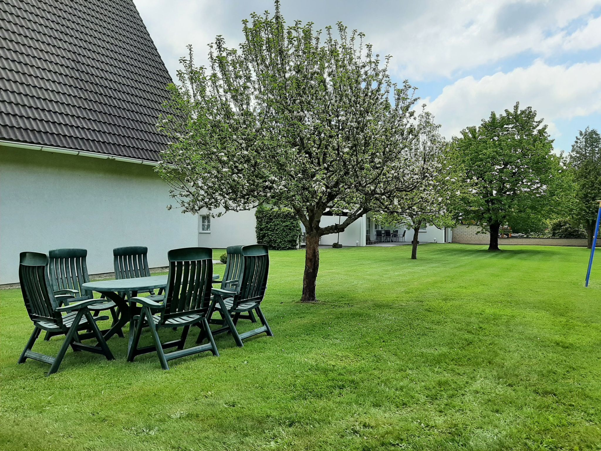 A patio with a table and chairs, a tree, and a building with a sloped roof.