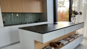 A modern kitchen with a central island, white cabinetry, and a view of autumn trees through the window. - Modernes Einfamilienhaus by Interhome (Fahrland)