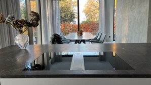 A modern kitchen with a reflective countertop, a dining area with a table and chairs, and a view of autumn trees through large windows. - Modernes Einfamilienhaus by Interhome (Fahrland)