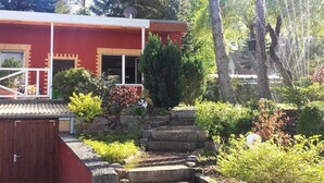 Ein rotes Gebäude mit Satellitenschüssel, umgeben von üppigem Grün und einer Steintreppe, die zu einer Holterrasse führt.
