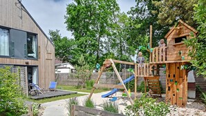 Een modern huis met een houten terras, een schommel en een poppenhuis.