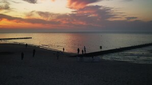 Een strand bij zonsondergang, mensen wandelen, en een pier die het water in reikt.