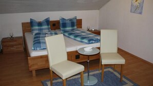 Ein kleines, ordentlich eingerichtetes Schlafzimmer mit einem Einzelbett, zwei Stühlen, einem kleinen Tisch und einem Nachttisch.