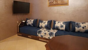 A living room with a sofa, a TV mounted on the wall, and a painting above the sofa. - Résidence Annaser 1 by Interhome (Agadir)