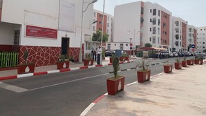A residential building with a red and white facade, a gated entrance, and potted plants along the sidewalk. - Résidence Annaser 1 by Interhome (Agadir)