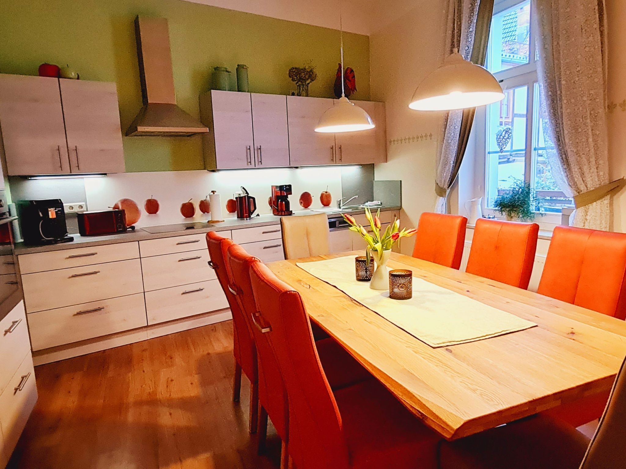 A modern kitchen with white cabinets, a wooden dining table, and orange chairs.