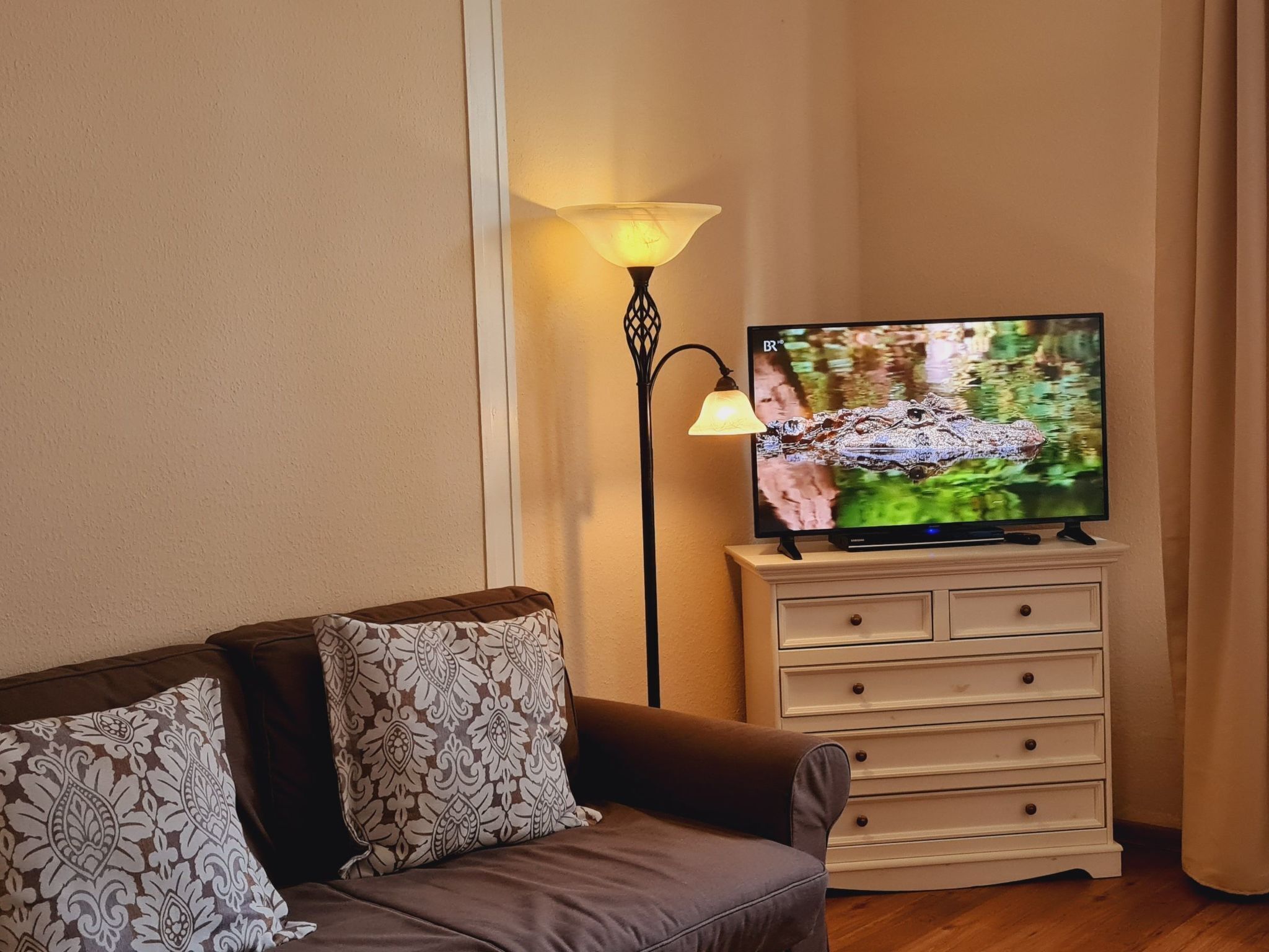 A living room with a sofa, a TV on a stand, a lamp, and a dresser.