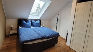 A bedroom with a skylight, a bed with blue bedding, a nightstand, a lamp, and a wardrobe. - Appartement mit Balkon by Interhome (Lasel)