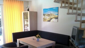 A modern living room with a wooden table, a sofa, a TV, and a painting of a landscape. - Kleines Ferienhaus mit Garten in Wismar by Interhome (Wismar)