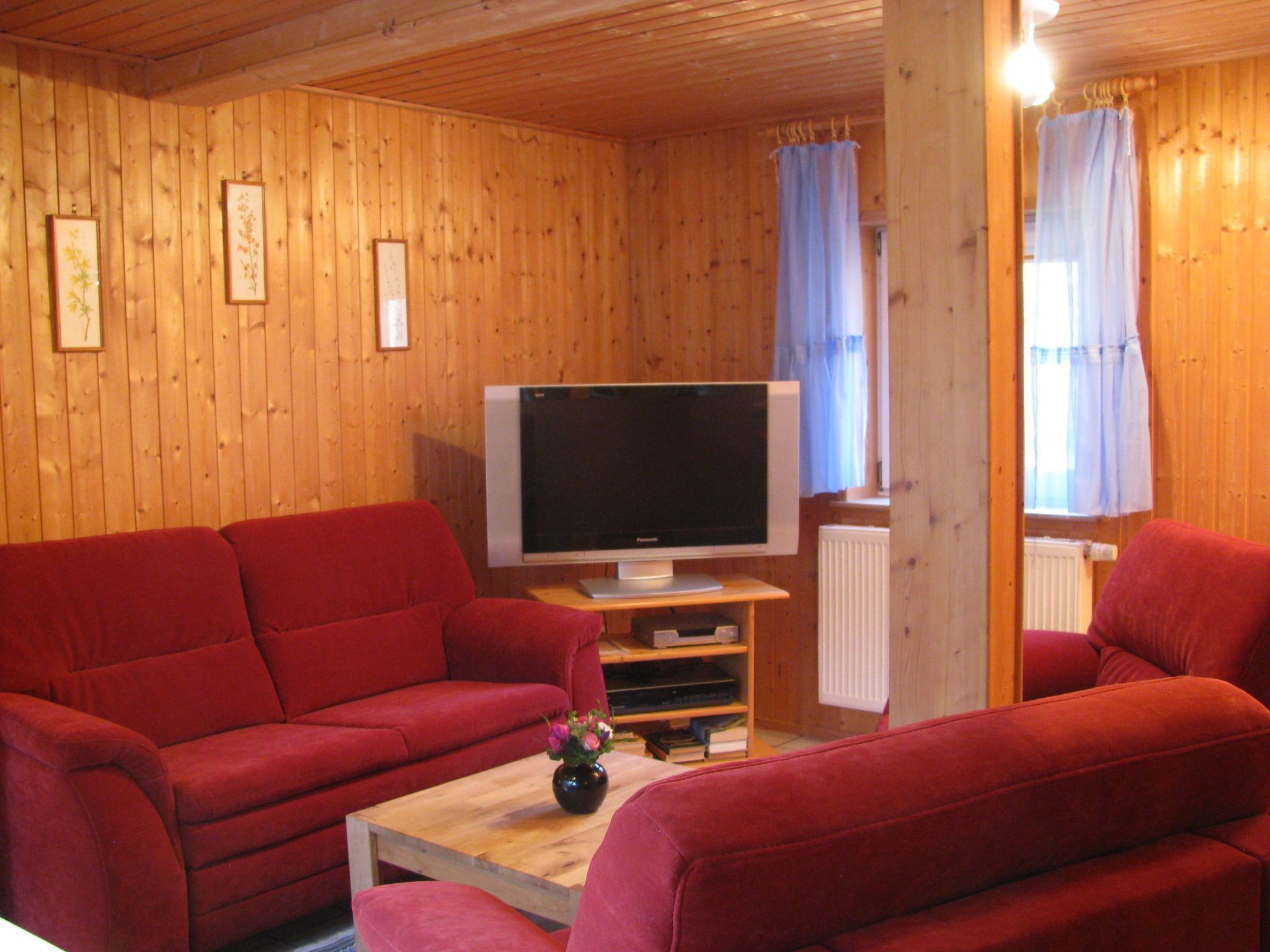 Een kamer met houten lambrisering, twee rode banken, een flatscreen televisie op een houten standaard en een kleine tafel met een vaas.