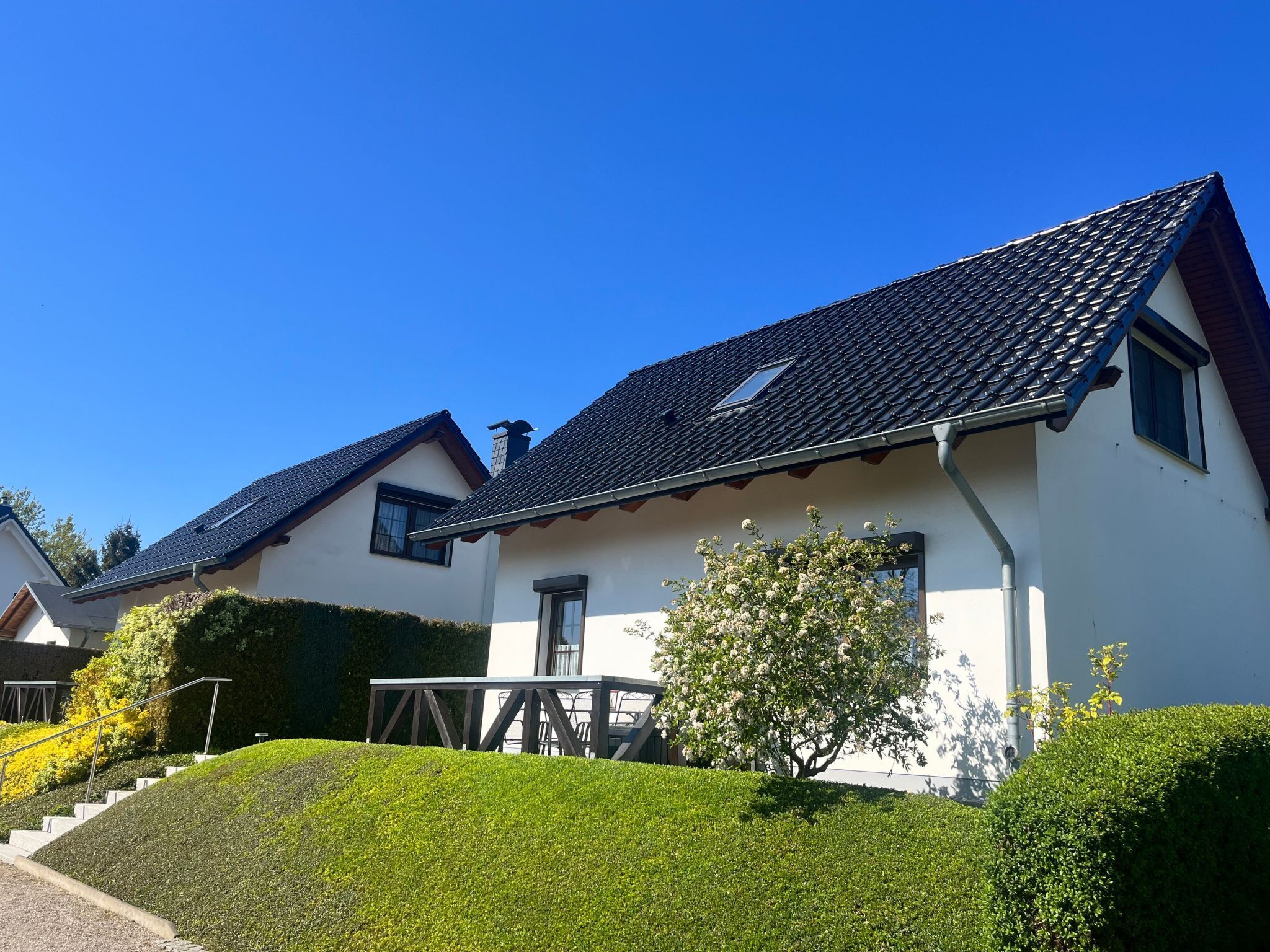 A modern two-story house with a dark tiled roof, white walls, and a small balcony.