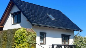 A two-story house with a dark tiled roof, white exterior walls, and a small balcony with a wooden railing. - FH Auf dem Holzweg by Interhome (Bansin)