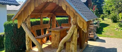 A wooden gazebo with a sloped roof, a table, and benches.