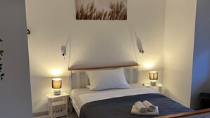 Een slaapkamer met een bed, bedlampen, een aan de muur hangend schilderij en een klein nachtkastje.