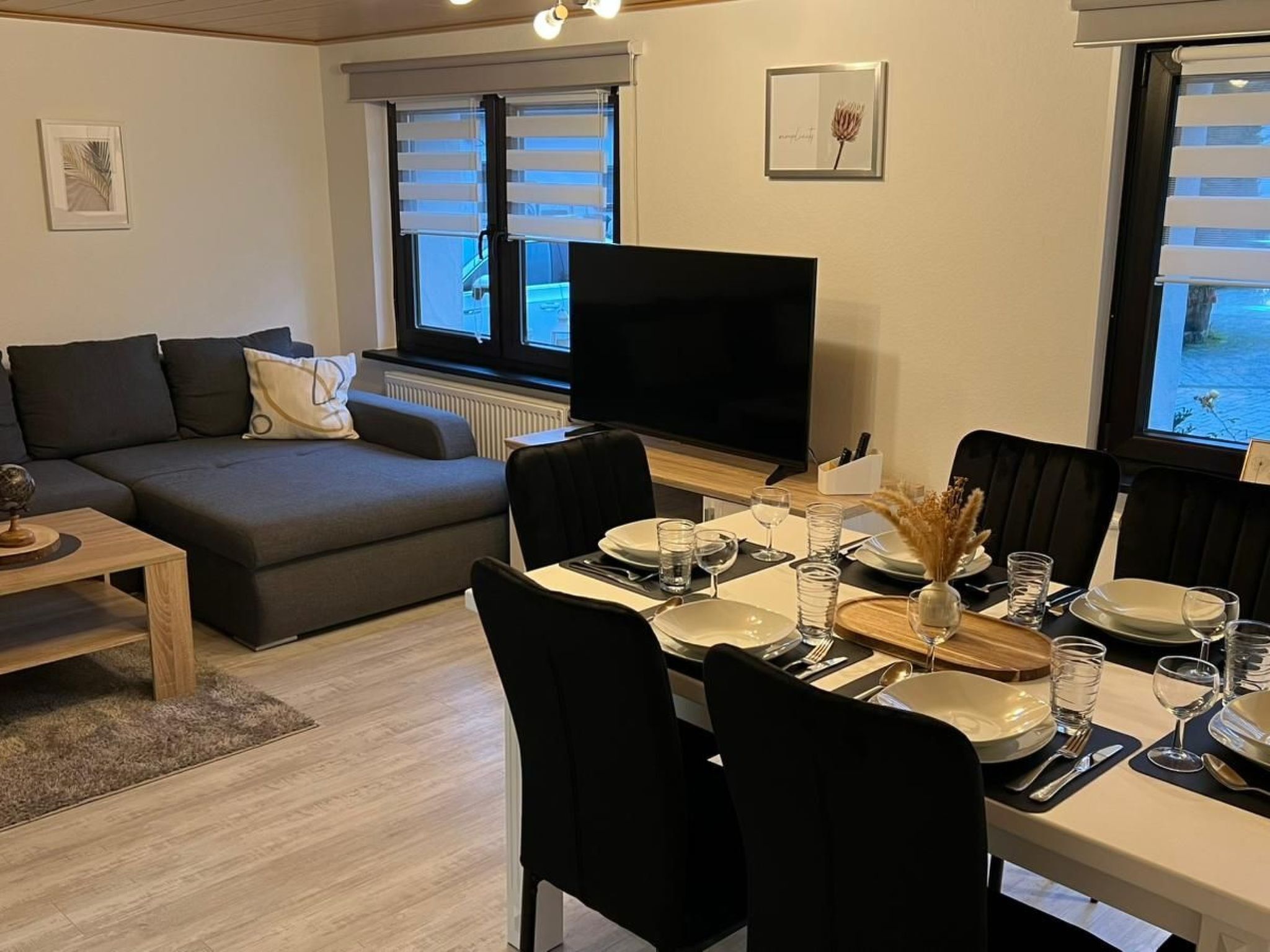 A modern living room with a sofa, a TV, and a dining area set for four.