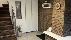 Een trap die naar een witte deur leidt, een bakstenen muur met een open haard, en een klein tafeltje met een fotolijst.