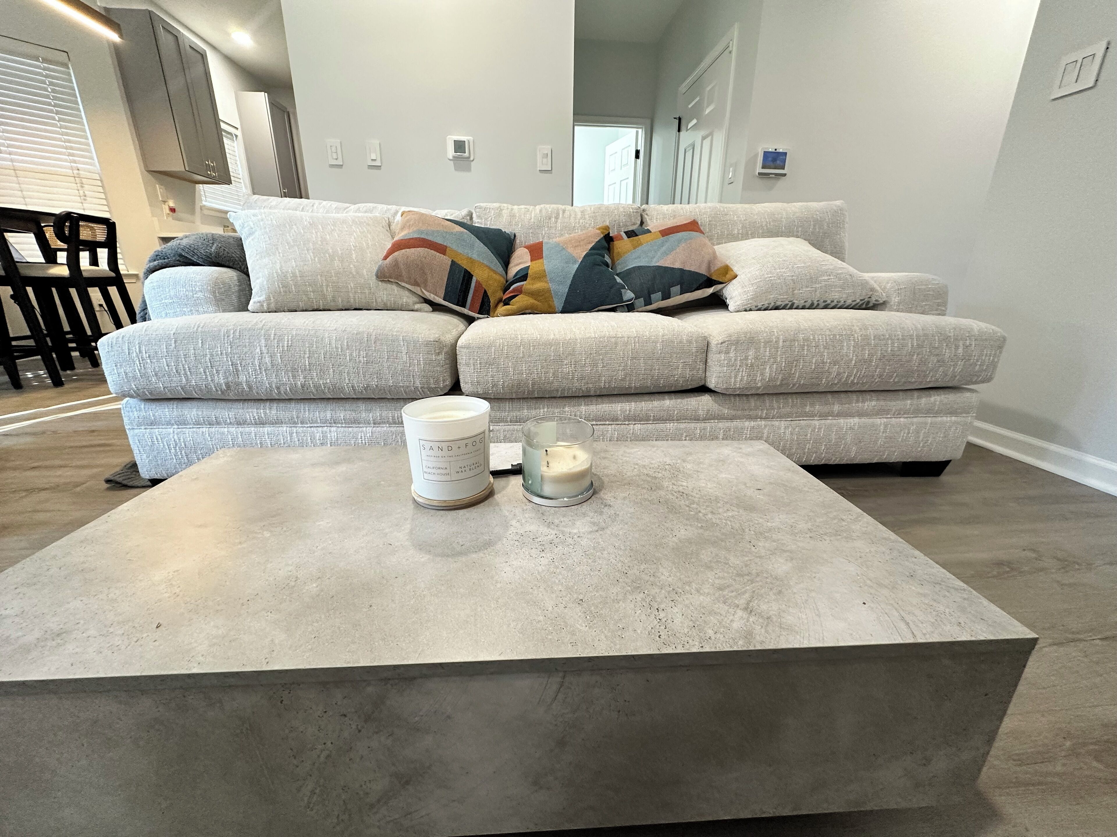 Un salon avec un canapé d’angle gris, une table basse en béton et une bougie blanche.