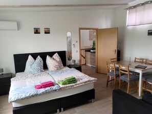 A bedroom with a bed, bedside tables, a mirror, a small kitchenette, and a dining area with chairs.