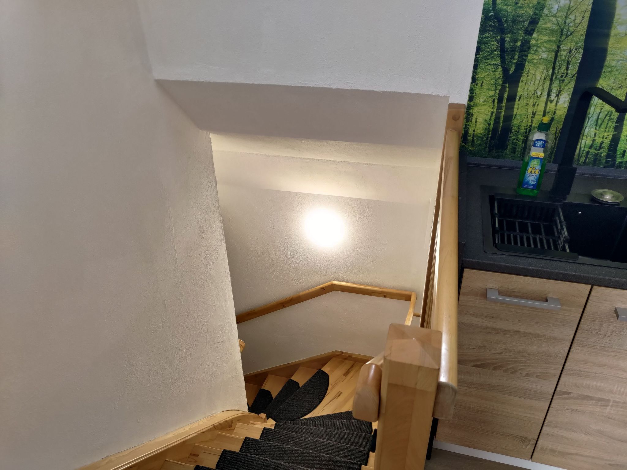A wooden staircase with a handrail, a window with a view of trees, and a bottle of cleaning product on the windowsill.