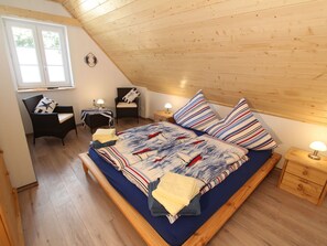 Et hyggeligt soveværelse med træloft, en seng med stribet sengetøj, en stol, et lille bord og et natbord med en lampe.