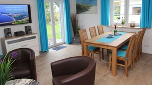A dining area with a wooden table, chairs, and a television displaying a welcome message. - Poseidon by Interhome (Seebad Altefähr)