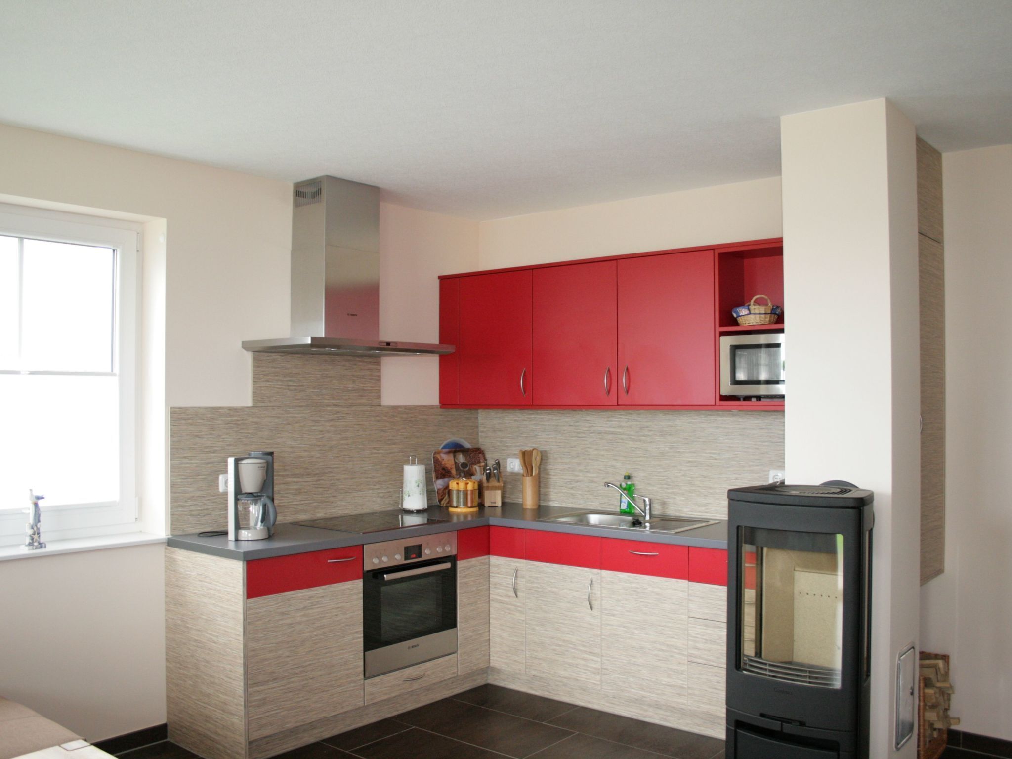 A modern kitchen with red cabinets, a built-in oven, and a microwave.