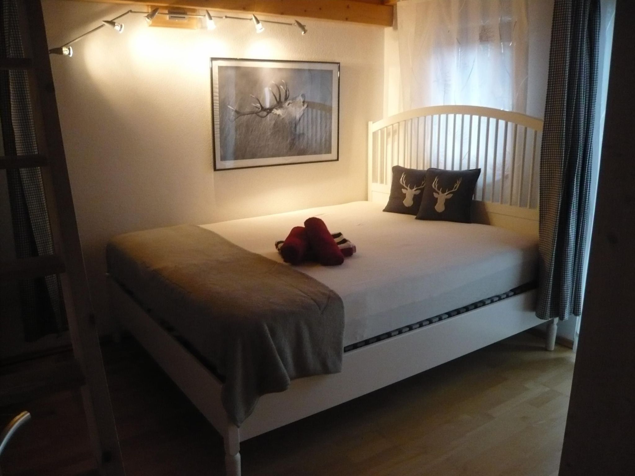 A bedroom with a bed, a headboard, a bedside table, a lamp, a framed picture, and a window with curtains.
