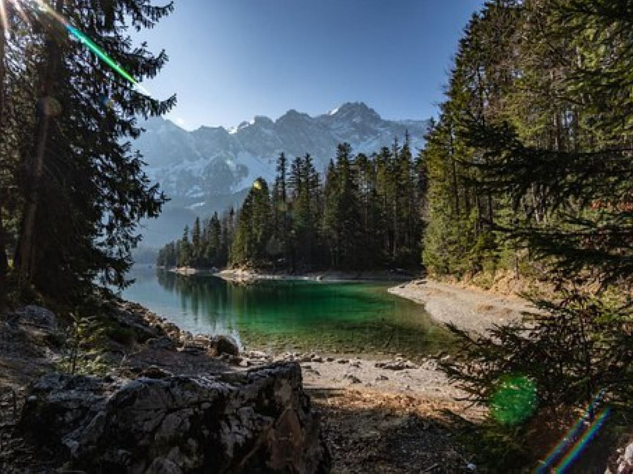 A mountainous landscape with a clear lake, dense forest, and rocky terrain.
