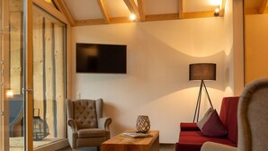 A living room with a wooden ceiling, a large flat-screen TV, a red sofa, a grey armchair, and a wooden coffee table. - Luxuschalet im Forstgut - Raum für wertvolle Zeit by Interhome (Regen)