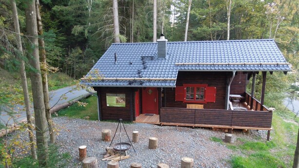 Een blokhut met een overdekt terras, een vuurkorf en een houten bank.