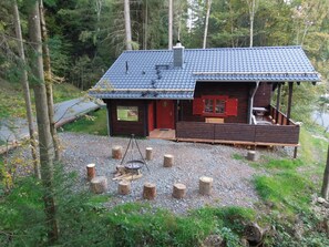 Eine Hütte mit überdachter Terrasse, Feuerstelle und einer Holzbank.