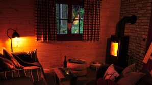 Een gezellig interieur van een blokhut, met houten details, een open haard, een raam met gordijnen en een lamp.