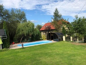 Ein Garten mit Swimmingpool, überdachter Sitzgelegenheit und einem Haus mit rotem Dach.