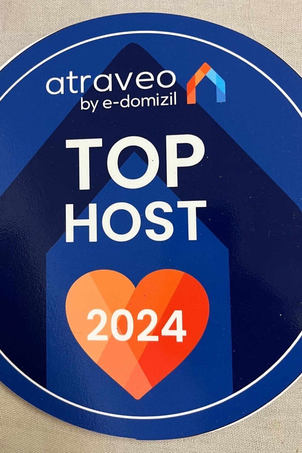 Pyöreä palkintomerkki, jossa on teksti ”atreveo by e-domizil TOP HOST 2024” ja talon kuvake.