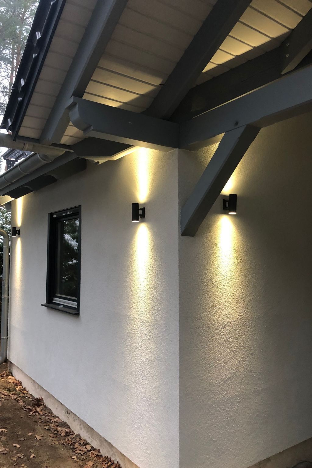 Ein Gebäude mit weißer Fassade, einem Fenster und drei Wandleuchten.