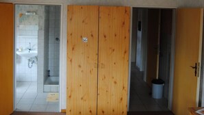 Quarto com guarda-roupa de madeira, cama com colcha florida e banheiro com pia e chuveiro.