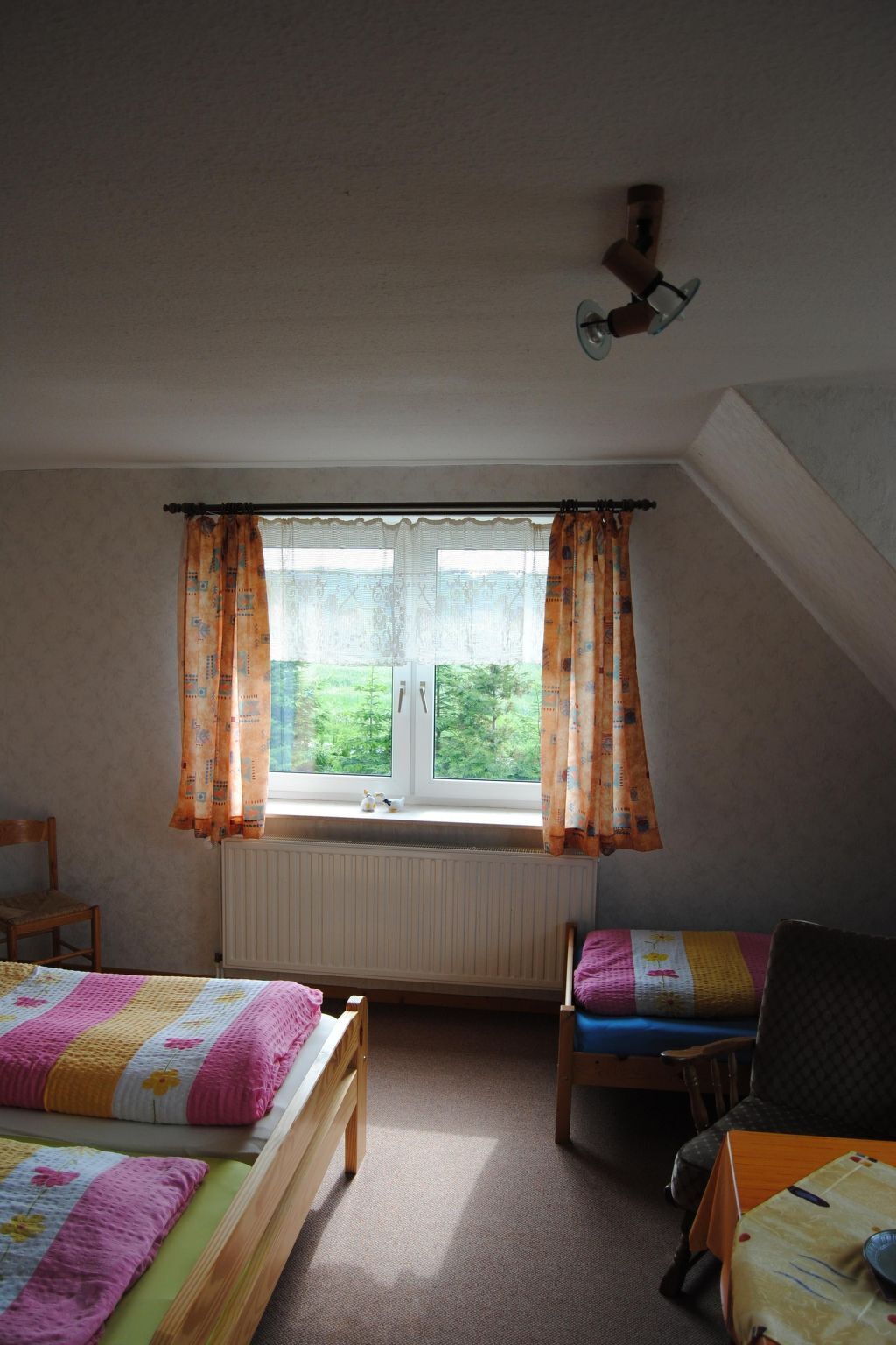 Une chambre avec deux lits, une fenêtre avec des rideaux, un radiateur et un ventilateur de plafond.