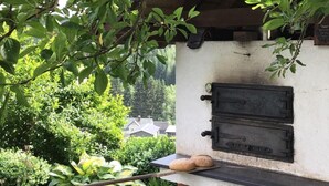 Un horno de ladrillo al aire libre con chimenea, rodeado de abundante vegetación y una bicicleta.