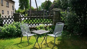 Une terrasse avec deux chaises en métal et une table, entourée d’une clôture en bois et de verdure.