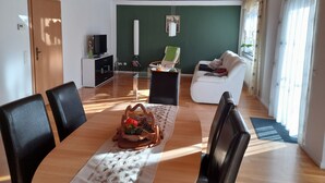 Un saló modern amb terra de fusta, un sofà blanc, una taula de dinar amb cadires, una televisió i una paret d'accent verd.