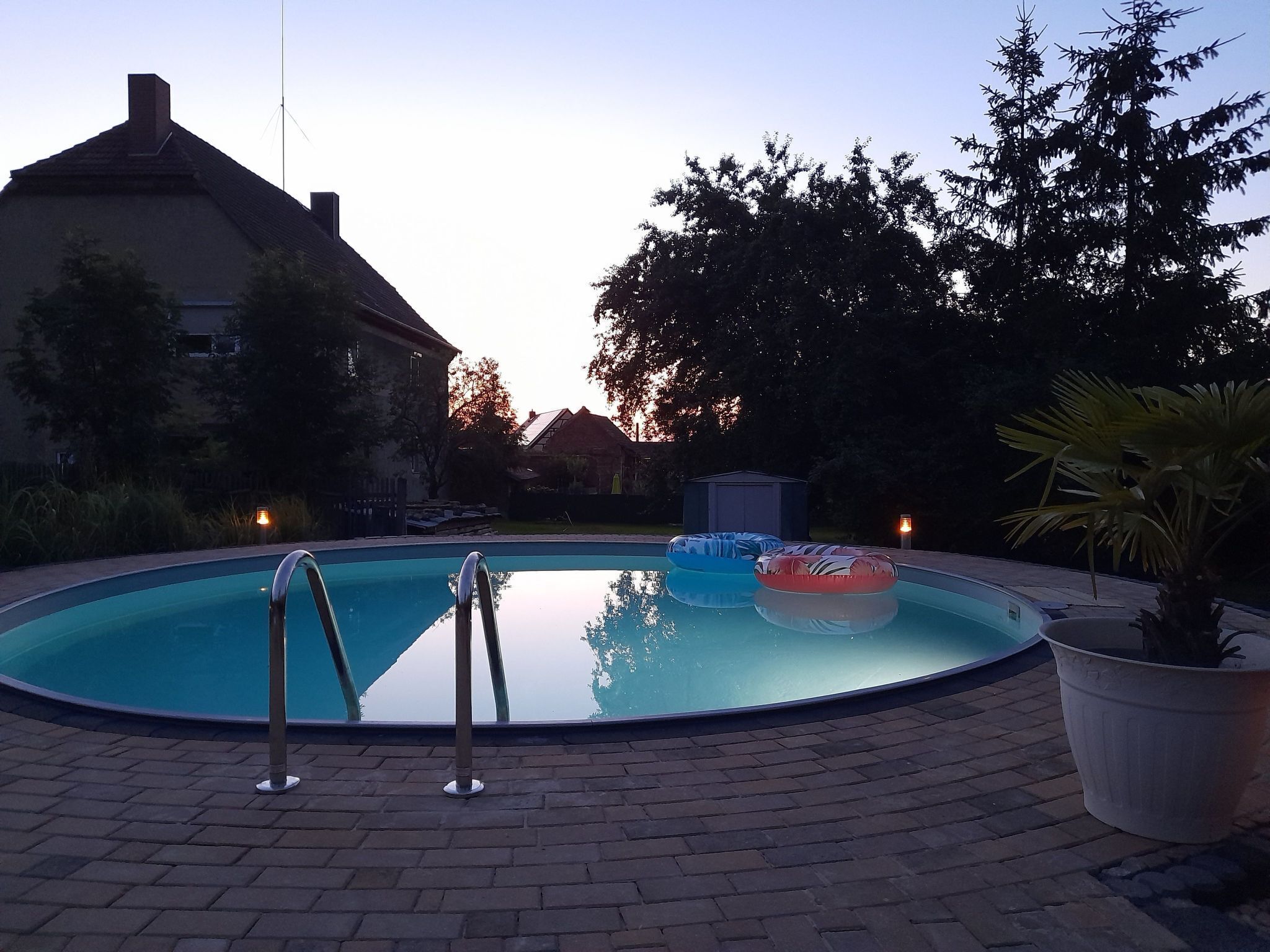 En swimmingpool med en metallstege, omgiven av en uteplats med ett stengolv.