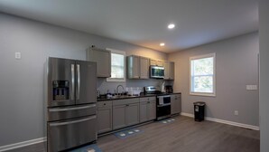 A modern kitchen with stainless steel appliances, grey cabinets, and a black trash can. - 4 Min to Downtown | 11 to Elon | Car Rental Avail. (Burlington)