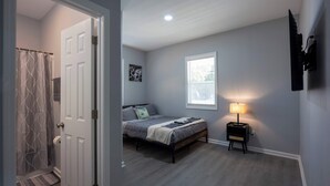 A bedroom with a bed, a nightstand, a window, and a door leading to a bathroom. - 4 Min to Downtown | 11 to Elon | Car Rental Avail. (Burlington)