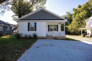 A single-story house with a gabled roof, white siding, and a front porch with a white railing.