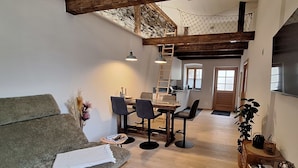 A cozy living area with a sofa, dining table, chairs, and a kitchen in the background. - Apartment Stadtmauerloft Gmünd by Interhome (Fischertratten)